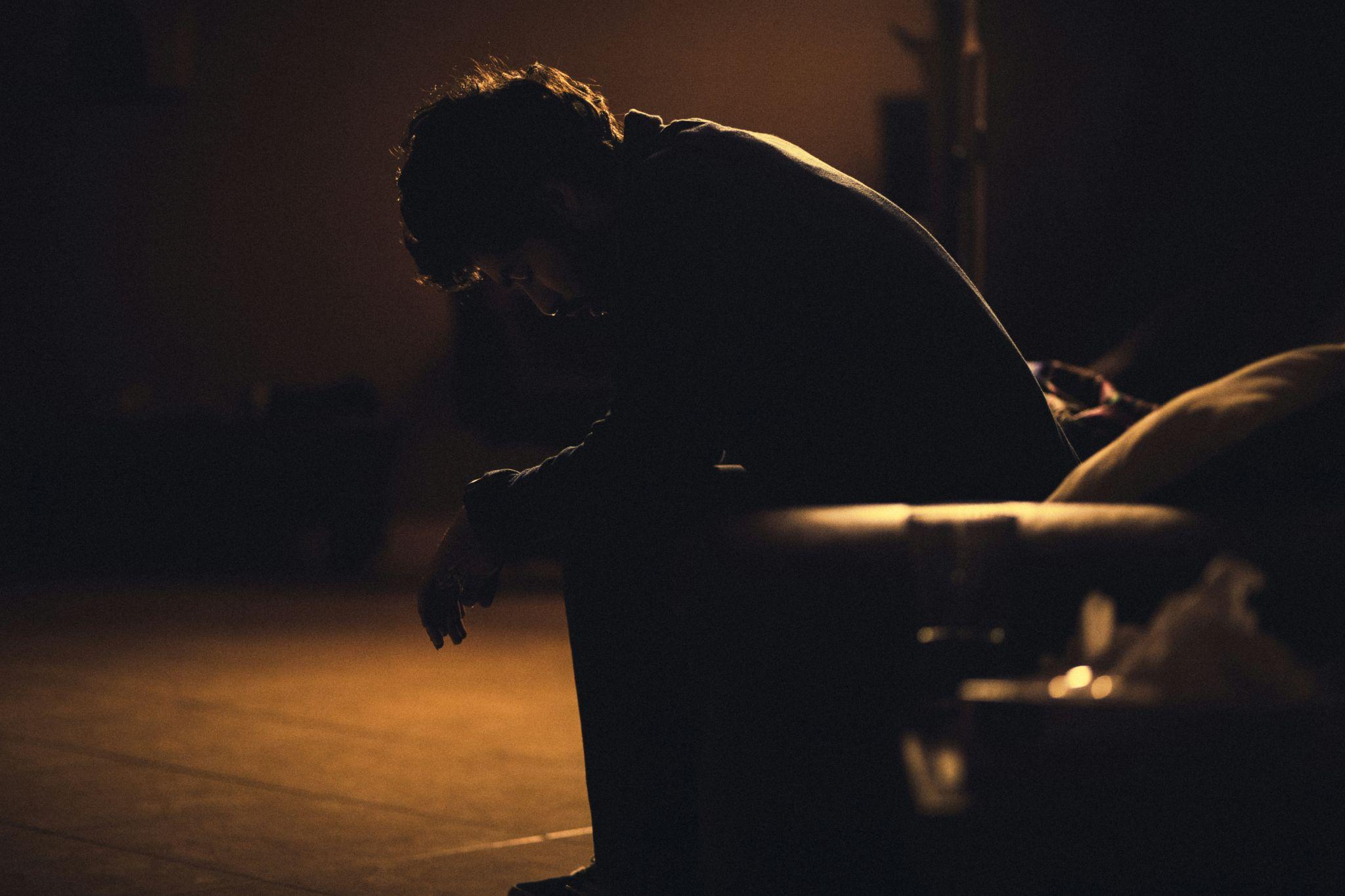 A person sitting in deep shadow, conveying visual themes of depression, loneliness, or mental exhaustion.